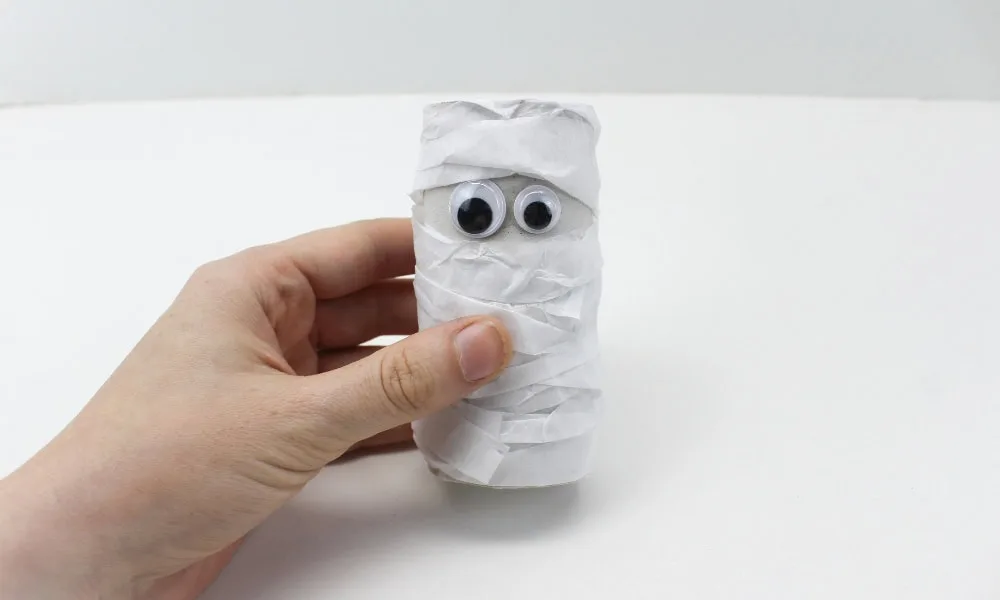 Momie d’Halloween fabriquée avec un rouleau de carton et du papier blanc