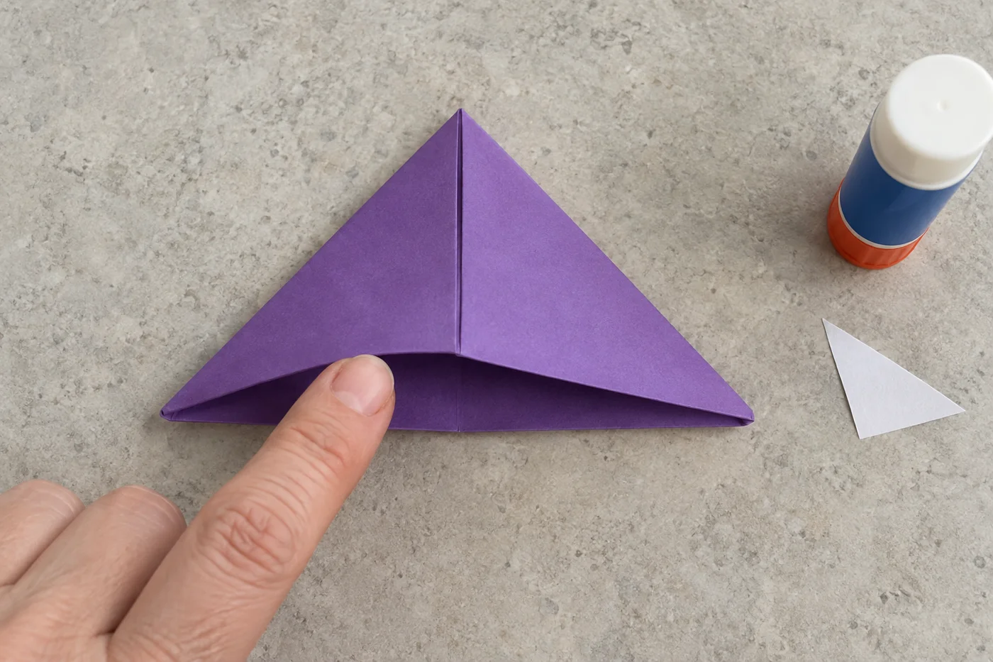 Doigt montrant l’ouverture d’une poche triangulaire en papier violet, prise de vue verticale