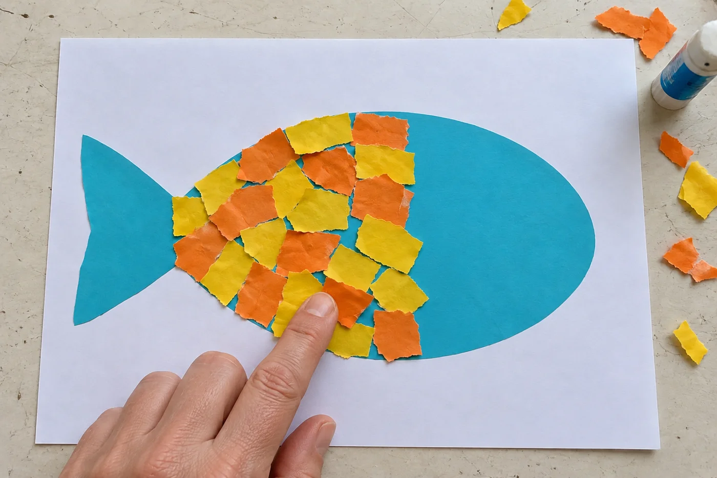 Collage partiel de morceaux jaunes et orange sur le corps du poisson, avec la tête et la queue encore bleues