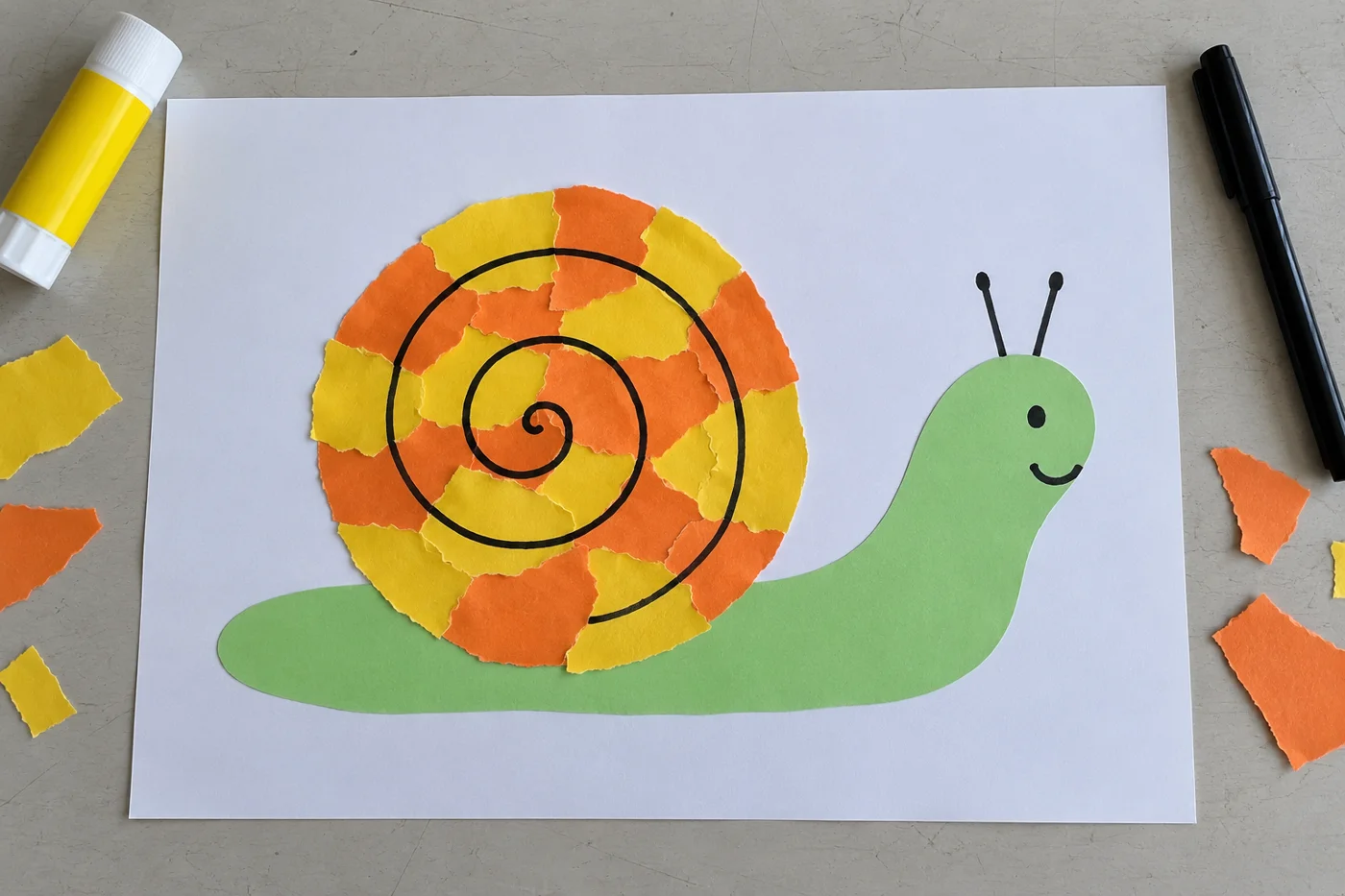 Escargot vert avec coquille jaune et orange en papier déchiré et spirale noire sur une feuille blanche, vue de haut