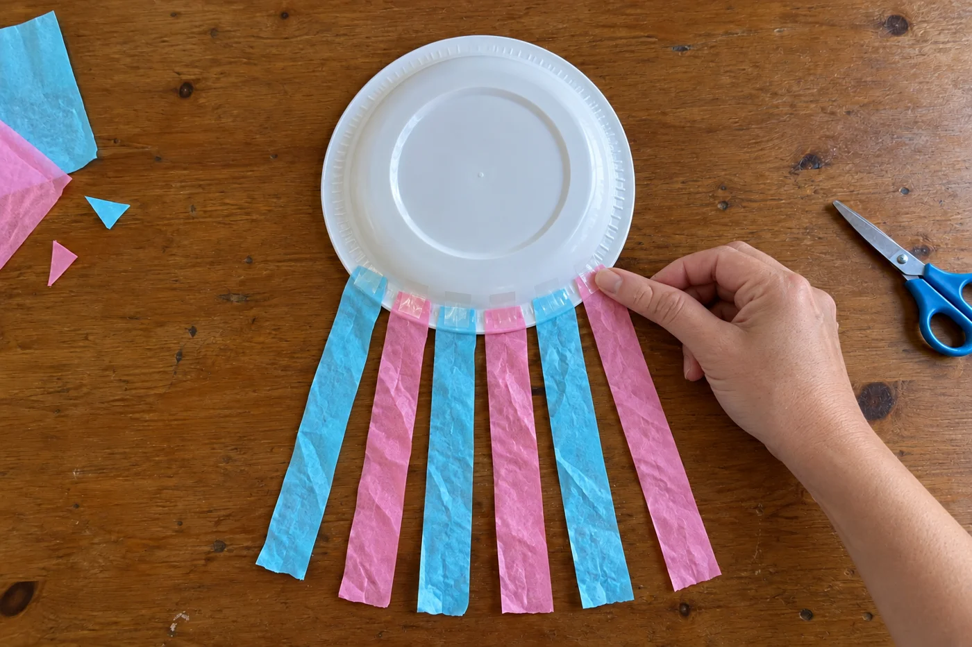 Six bandes alternées bleues et roses fixées au ruban adhésif sur le bord inférieur du dos d’une assiette, vue de haut