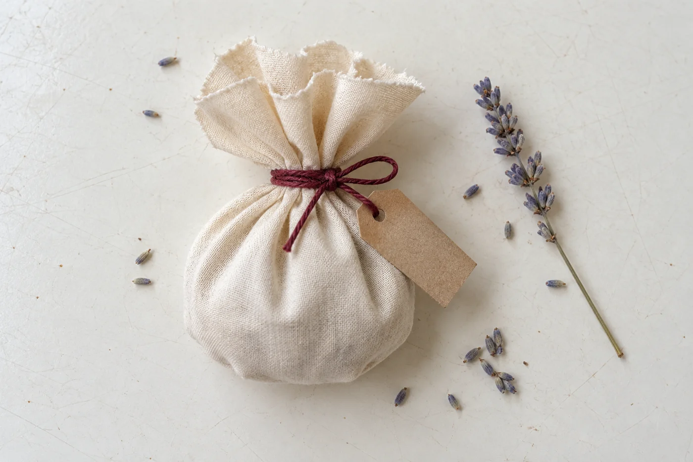 Petit sachet de lavande en coton écru noué par une ficelle bordeaux et muni d’une étiquette kraft, vue de haut