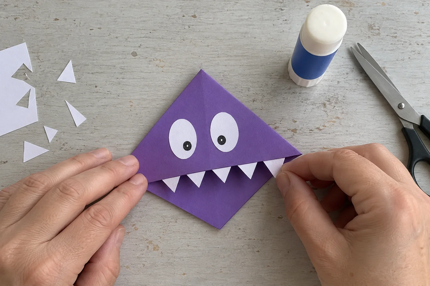 Mains collant les dents et deux yeux en papier blanc sur un marque-page monstre violet vu de haut