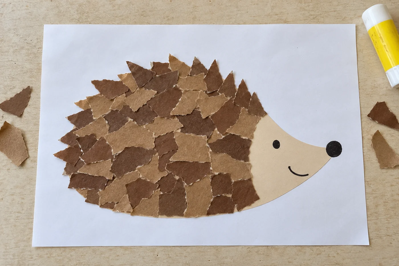Hérisson souriant en papier beige et morceaux de papier brun déchiré sur une feuille blanche, vu de haut
