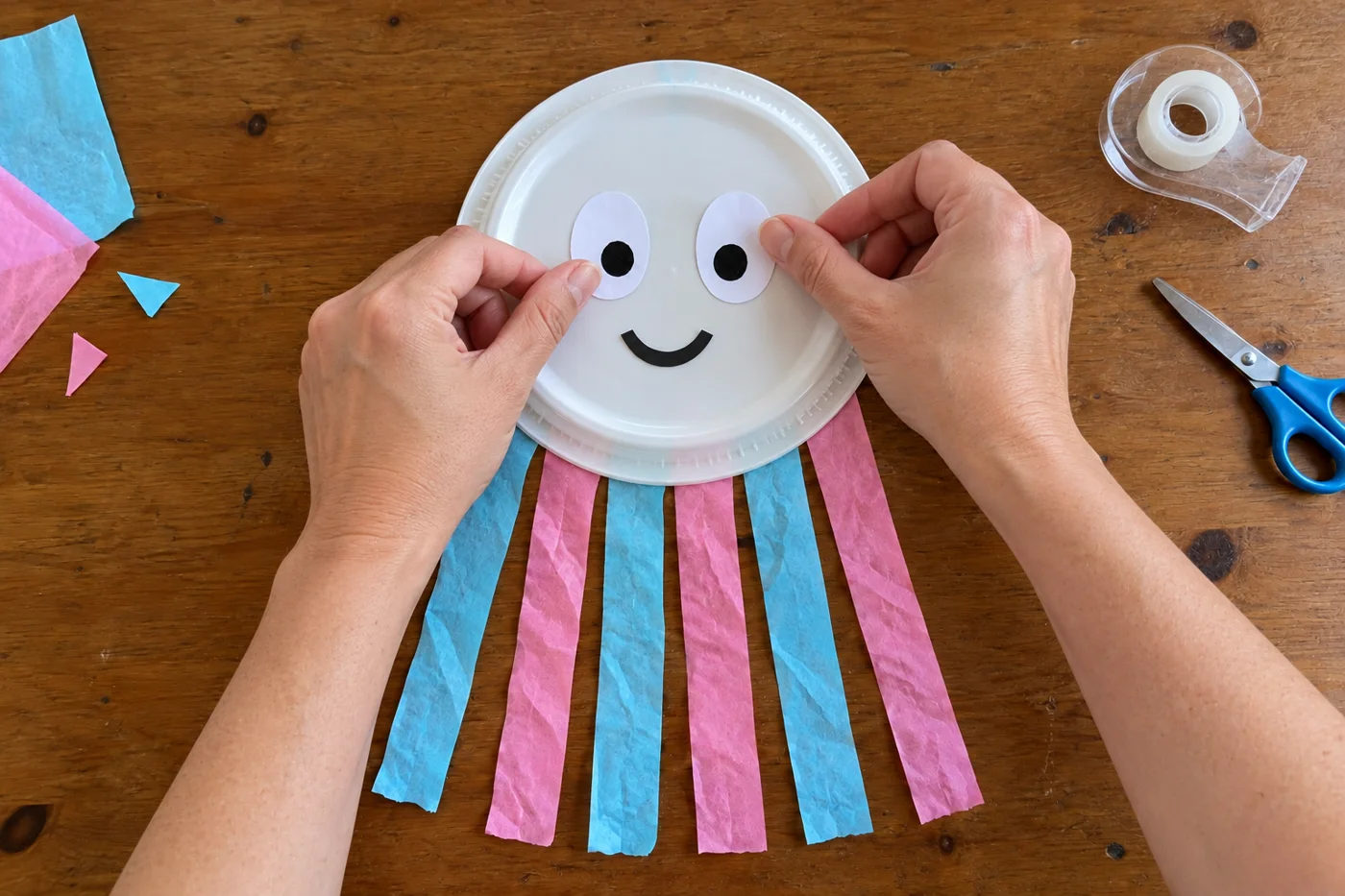 Mains fixant deux grands yeux de papier et un sourire sur l’assiette, avec les six tentacules déjà attachés